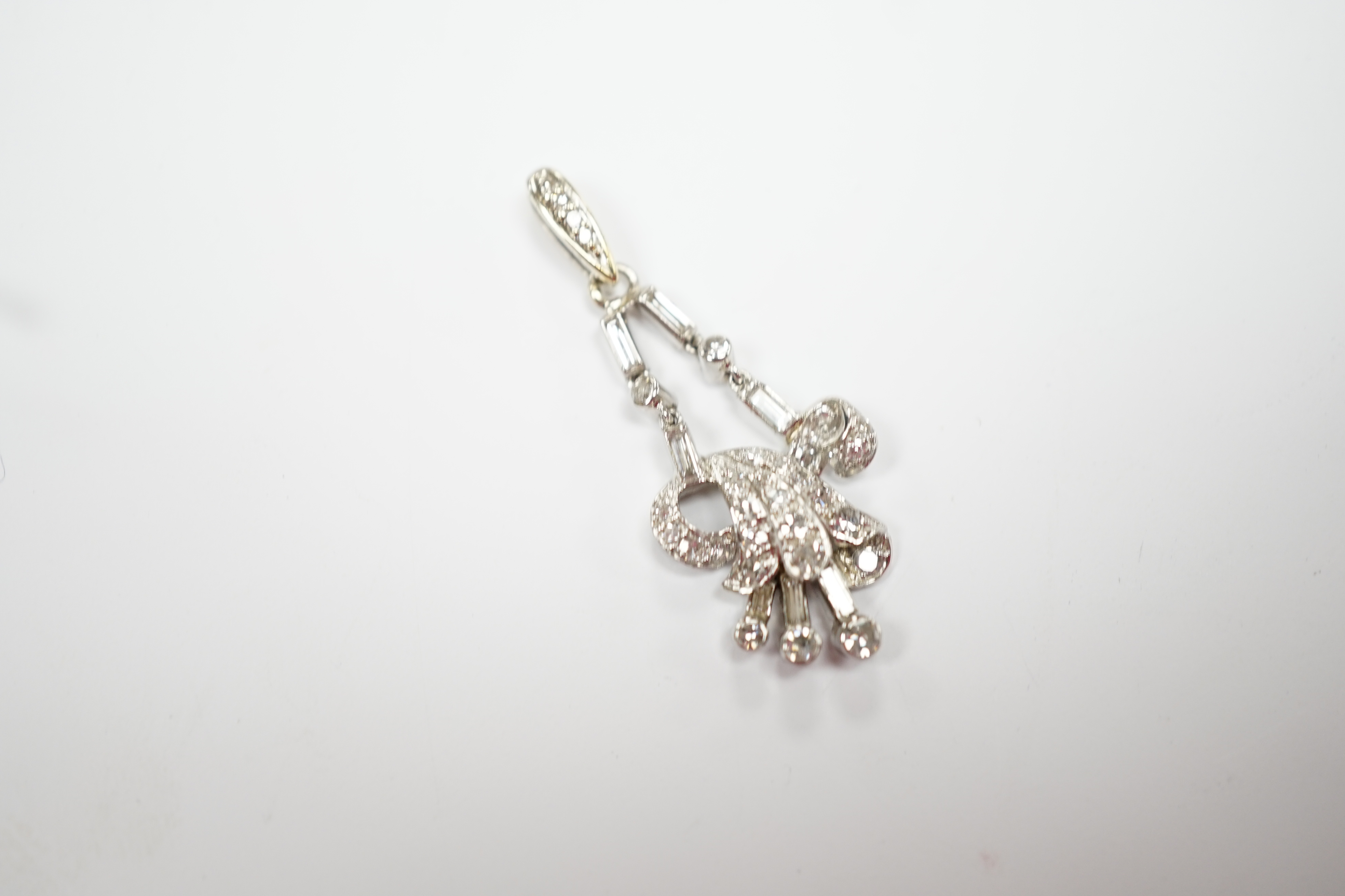 A white metal baguette and round cut diamond cluster set scroll pendant, overall 33mm, gross weight 3.6 grams.